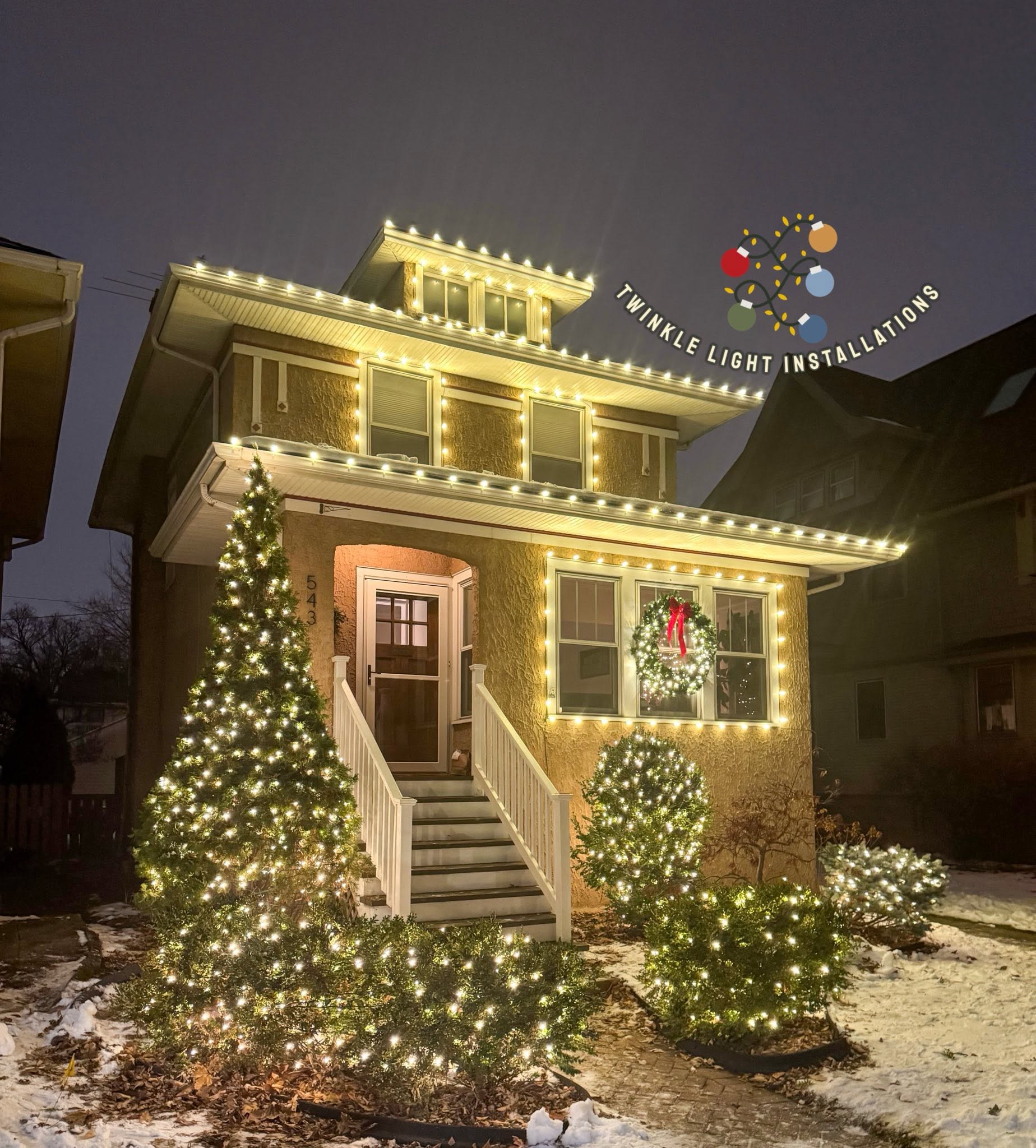 Home with warm white Christmas lights, illuminated greenery, and a wreath