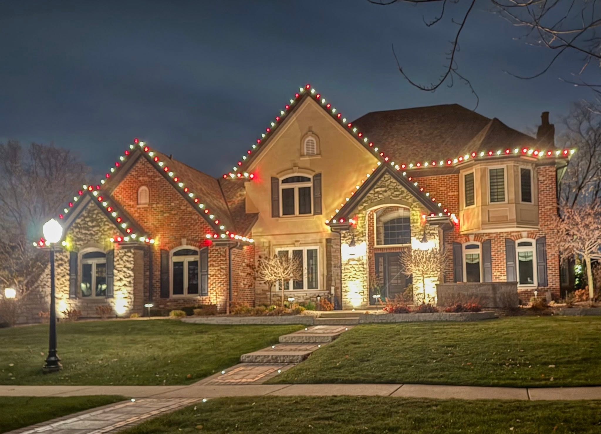 Large home with alternating red and warm white Christmas roofline lights