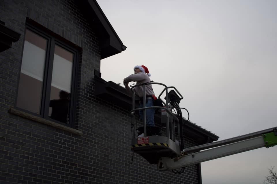 Twinkle Light Installations team member in a Santa hat installing lights from a lift